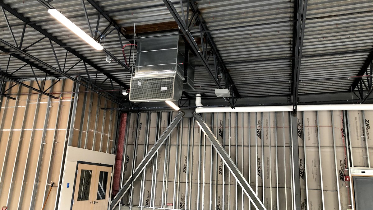 Commercial indoor air handler and ductwork installed above a partially finished space with exposed framing and ceiling structure.