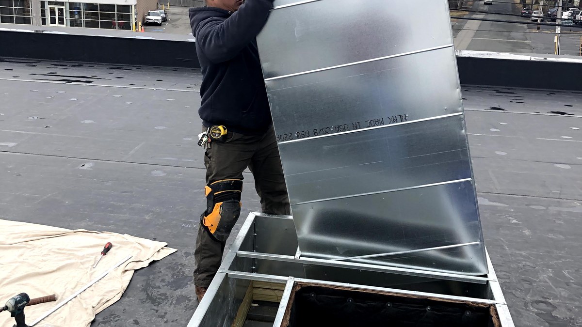 Technician handling rooftop HVAC ductwork on a commercial flat roof.