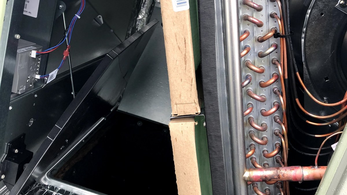 Open commercial HVAC air handler showing a coil, copper refrigerant tubing, wiring, and internal service access.