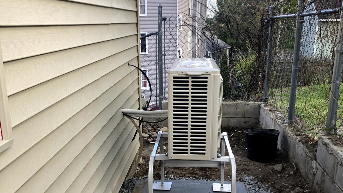 Outdoor heat pump or AC condenser installed beside a home with wall clearance and service space.