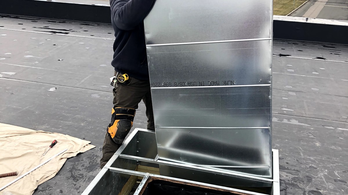 Technician positioning sheet metal ductwork at a commercial rooftop HVAC opening.