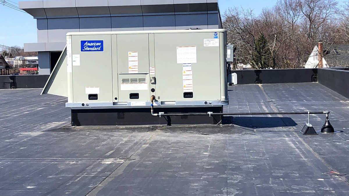 Commercial rooftop HVAC unit installed on a flat roof with gas piping and roof supports visible.