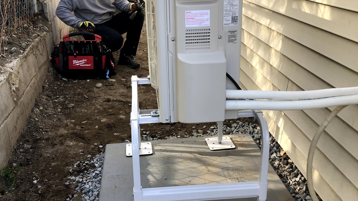 Technician working beside an outdoor mini-split heat pump unit near a home