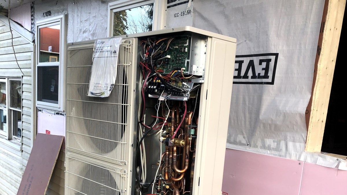 Open outdoor mini-split heat pump unit with refrigerant service hoses and internal components visible during startup checks.